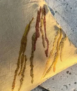 Hand-embroidered linen throw pillow with organic rust and green stitching on stone.